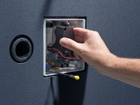 A hand is inserting a component into an open electrical box set against a textured background.