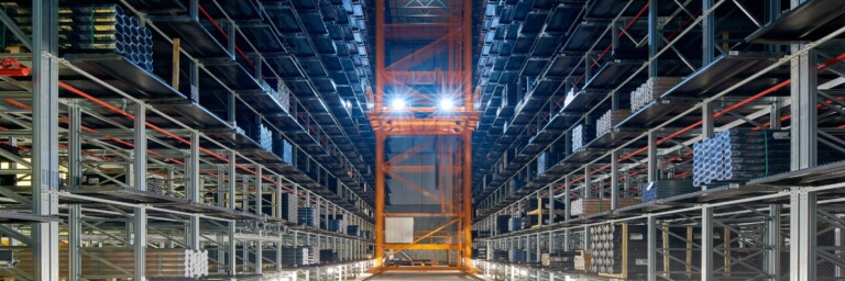 Ein grosser, gut beleuchteter Lagerraum mit hohen Regalen, die mit verschiedenen Materialien gefüllt sind, und einem automatisierten Transportsystem in der Mitte.
