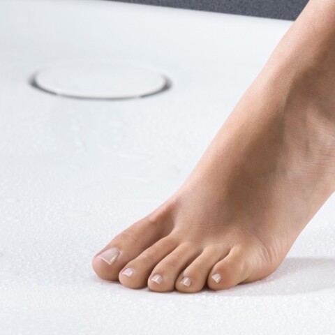 A bare foot stepping onto a white shower surface with water droplets.