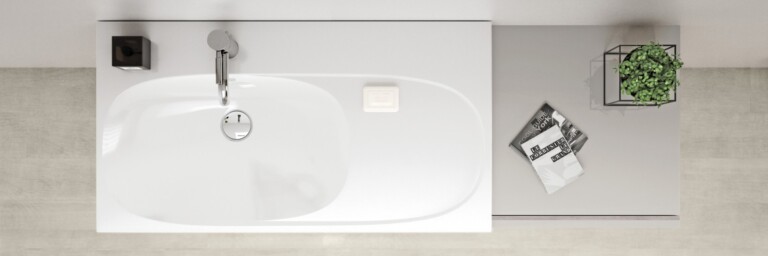 Eine modernes, weisses Waschbecken mit einer silbernen Armatur, daneben ein kleiner Topf mit einer Pflanze und zwei Zeitschriften auf einem grauen Ablagetisch.