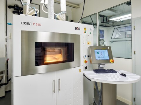 Eine moderne 3D-Druckmaschine in einem technischen Raum, mit einem Bildschirm und Bedienelementen.