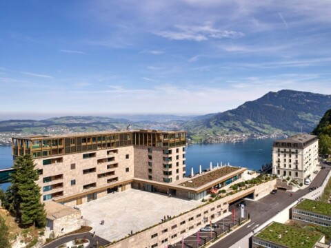 Moderne Gebäude mit Terrassen und Panoramablick auf einen See und umliegende Berge.