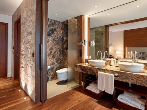 Modernes Badezimmer mit Holzfussboden, marmorierten Wänden, Doppelwaschtisch und Glasdusche.