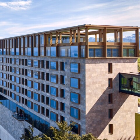 Moderne Hotelarchitektur am Hang mit Blick auf einen See und umliegende Berge.