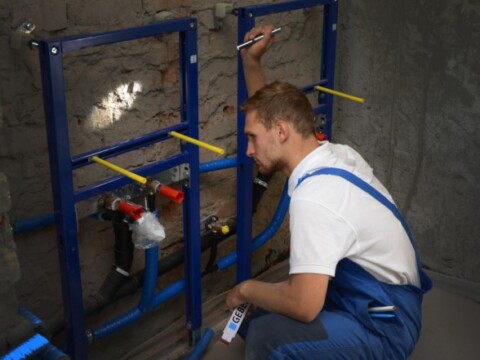 Ein Handwerker in blauen Latzhosen arbeitet an einer Wandinstallation.