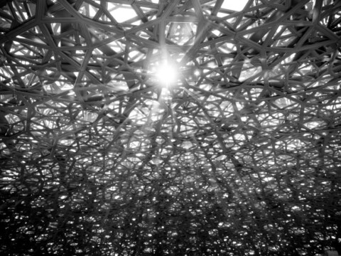 A textured, abstract black and white image featuring a lattice-like structure with light shining through, creating intricate shadows.