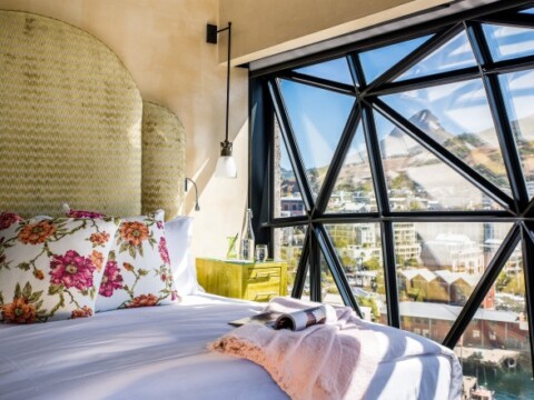 Modern bedroom featuring a large geometric window with mountain views, floral pillows, and a cozy bed.