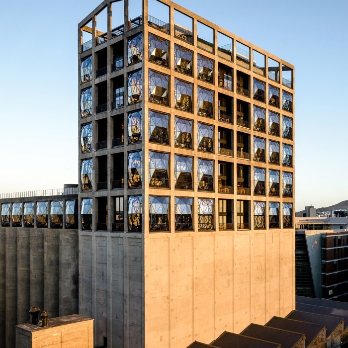 A modern building with a distinct geometric design, featuring large windows and set against a mountain backdrop.