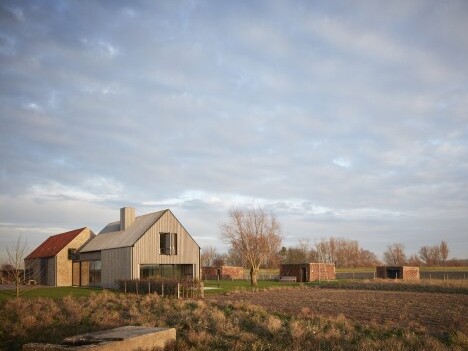Zwei moderne Häuser aus Holz und Metall stehen in einer ländlichen Umgebung unter einem bewölkten Himmel.