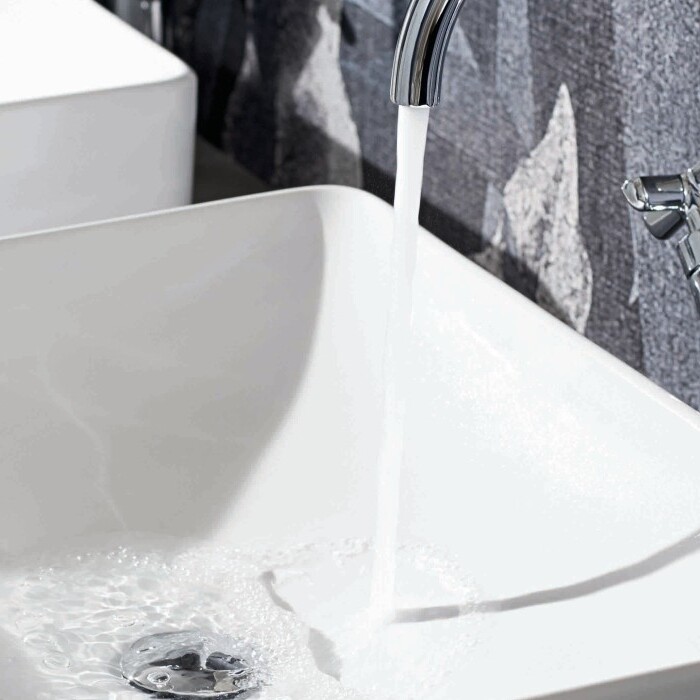 Zwei moderne, weisse Waschbecken vor einer Wand, eines mit fliessendem Wasser.