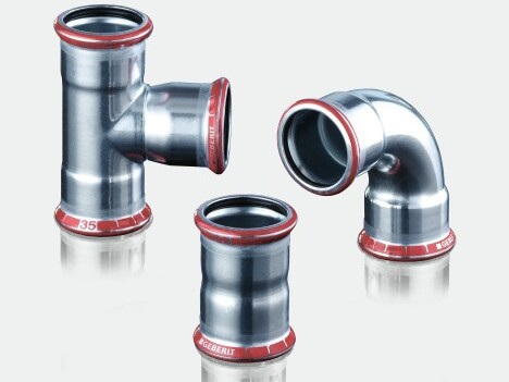 Drei Metallrohrverbindungen mit roten Dichtungen: ein T-Stück, ein gerader Verbindungsschlauch und ein 90-Grad-Bogen.