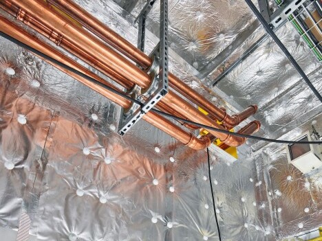Kupferrohre, die an einem mit Isolierung bedeckten Deckenpaneel befestigt sind, mit elektrischen Leitungen in der Nähe.