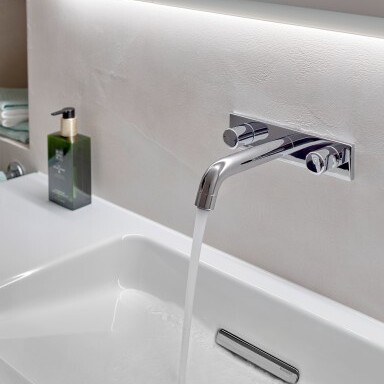 A modern bathroom sink with a shiny chrome faucet dispensing water, and a green soap bottle nearby.