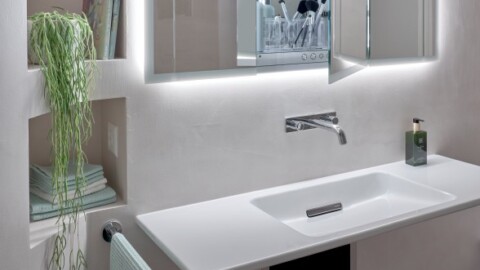Modern bathroom interior featuring a sleek sink, wall-mounted faucet, illuminated mirrors, and decorative plant.