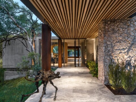 Moderne Architektur mit einem überdachten Eingangsbereich, Steinmauer und Skulptur.