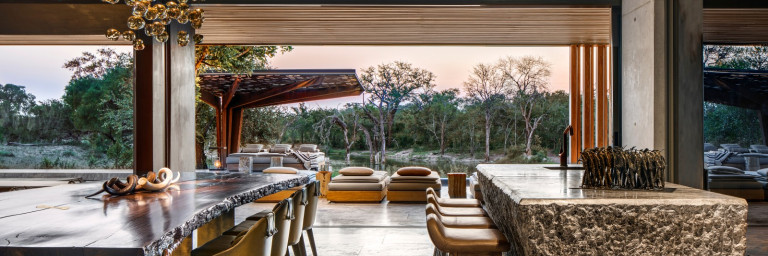 Moderner Essbereich mit Tageslicht, einem grossem Holztisch, stilvollen Sitzgelegenheiten und Blick auf die üppige Vegetation draussen.