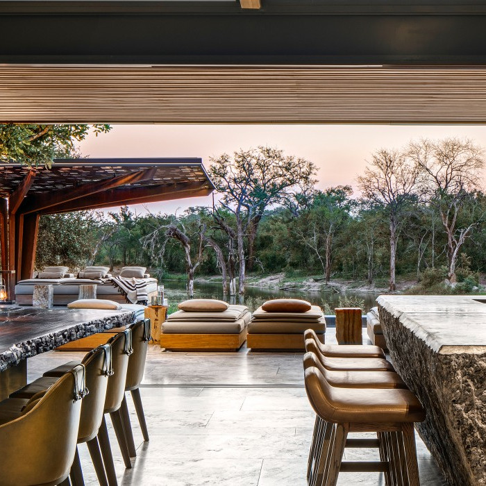 Moderner Essbereich mit Tageslicht, einem grossem Holztisch, stilvollen Sitzgelegenheiten und Blick auf die üppige Vegetation draussen.