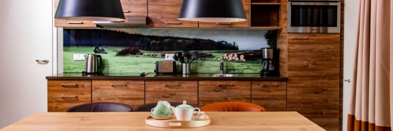 Modern kitchen with wooden cabinetry, a large dining table and a scenic wallpaper of greenery.