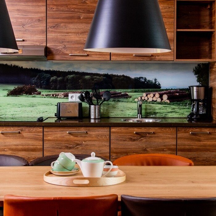 Modern kitchen with wooden cabinetry, a large dining table and a scenic wallpaper of greenery.