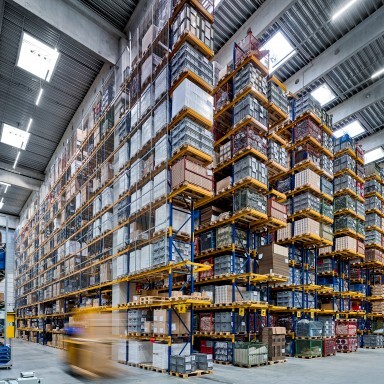 A large warehouse interior filled with tall shelves stacked with boxes and pallets.
