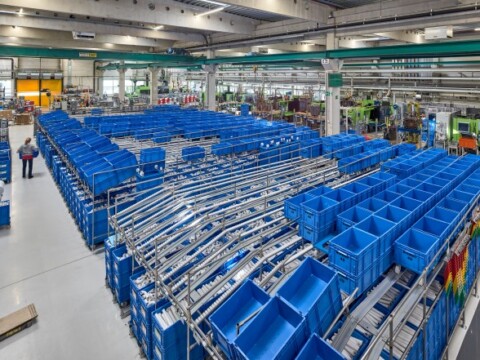 A large warehouse interior filled with blue storage bins organized on metal racks, with a few people in the background.
