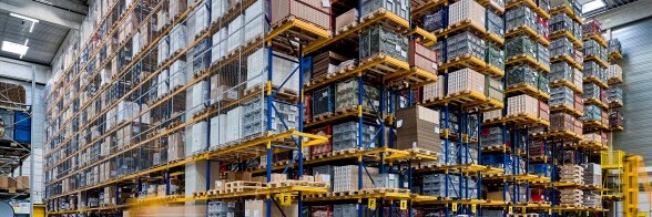 A large warehouse interior filled with tall shelves stacked with boxes and pallets.