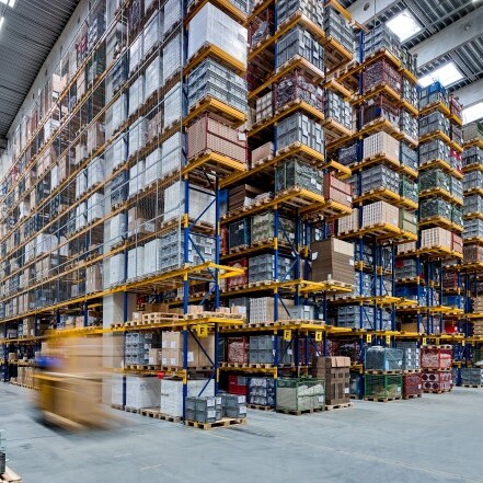 A large warehouse interior filled with tall shelves stacked with boxes and pallets.