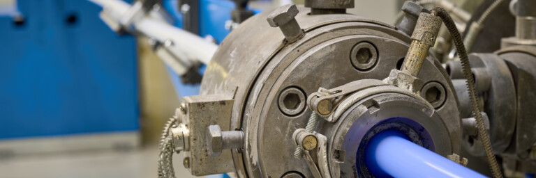 A close-up view of machinery with a blue pipe and industrial equipment in the background.
