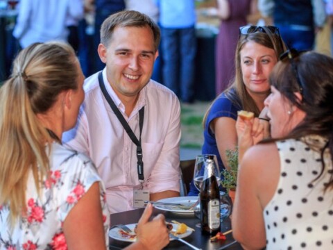 A group of four people engaging in conversation at an outdoor gathering, with food and drinks on the table.