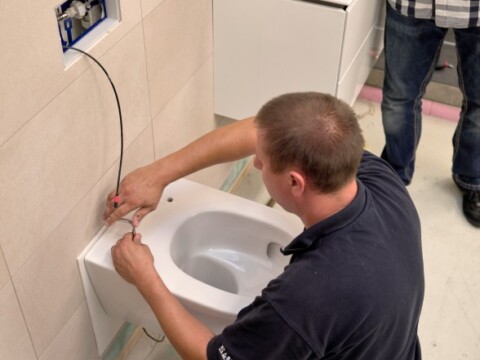 Ein Handwerker installiert eine wandhängende Toilette und verbindet dabei Drähte in einem modernen Badezimmer.