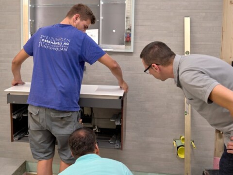 Drei Handwerker, die einen Badezimmerwaschtisch installieren und die Ausrichtung prüfen.
