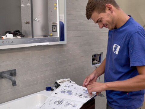 Ein junger Mann in blauer Kleidung steht an einem Waschbecken und sieht sich Anweisungen zum Installieren an.