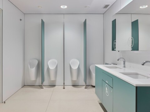 A modern bathroom interior featuring three urinals and a sink with a mirror, designed with light colors and minimalistic elements.