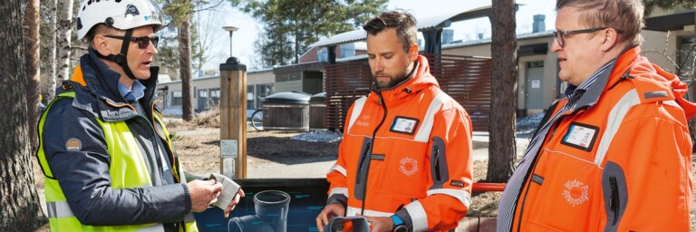 Drei Personen in leuchtender Arbeitskleidung stehen im Freien und diskutieren.