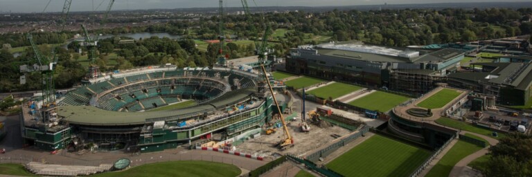 Blick auf das Wimbledon-Stadion im Bau mit Kränen und grünem Rasen in der Umgebung.