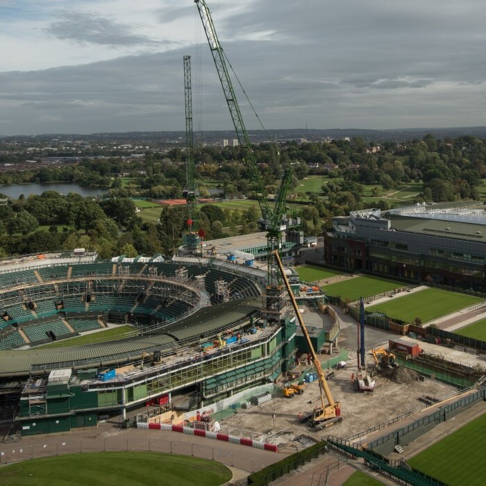 Blick auf das Wimbledon-Stadion im Bau mit Kränen und grünem Rasen in der Umgebung.