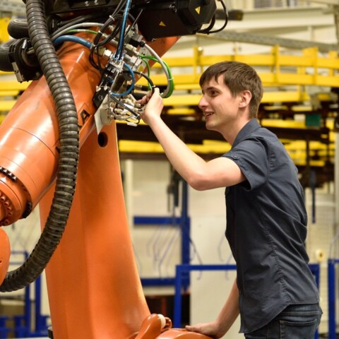 A person adjusting a large orange robotic arm in an industrial setting.