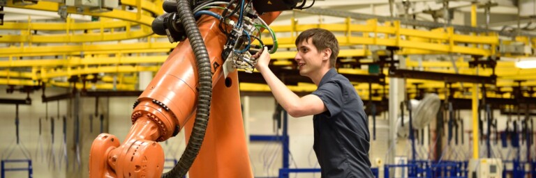 Ein Techniker arbeitet an einem grossen, orangefarbenen Industrieroboter in einer Fertigungsanlage.