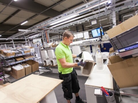 A worker in a bright green shirt operates equipment in a warehouse filled with packages and boxes.
