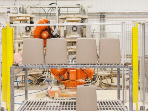 A manufacturing setup, a metal shelf and an orange robotic arm in the background.
