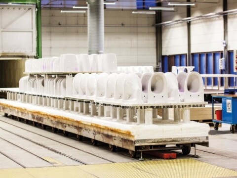 A row of white toilet bowls on a conveyor in a manufacturing facility.
