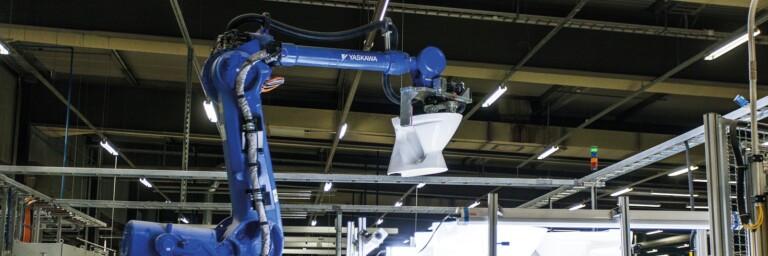An industrial blue robotic arm holding a white toilet.