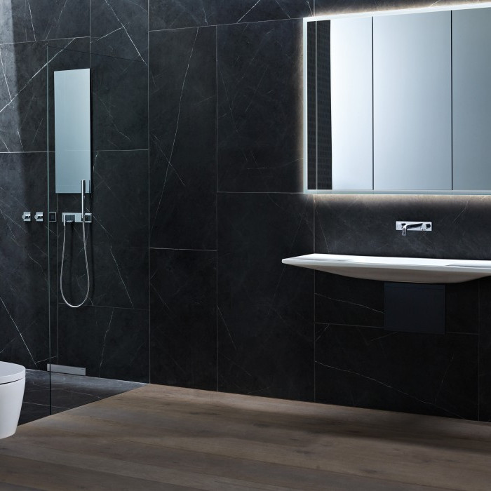 Modern bathroom with dark tiled walls, a sleek toilet, a wall-mounted sink and a large mirror.
