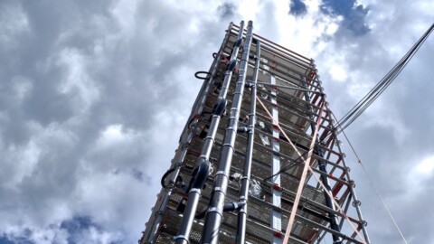 A tall construction scaffold with metal pipes against a cloudy sky.