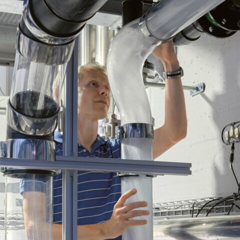 A person adjusting equipment in a laboratory with tubes and machinery visible in a modern setting.
