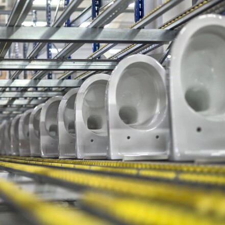 A row of white toilets positioned on metal shelves in a warehouse setting.