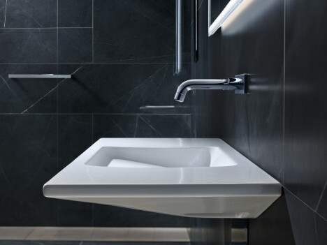 Modernes, wandmontiertes Waschbecken mit minimalistischem Design in einem eleganten, dunklen Badezimmer.