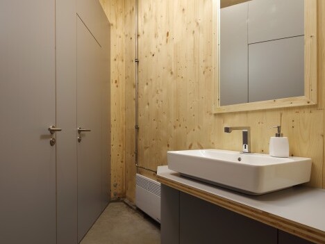 Modern bathroom interior featuring wooden walls, a minimalistic sink with a rectangular basin, a wall-mounted mirror, and two doors.