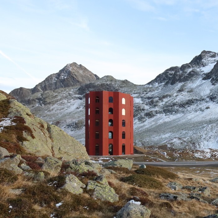 Two unique, colorful towers, one red and one yellow, situated in a mountainous landscape with patches of snow.
