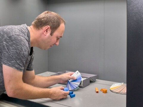 A man is selecting color samples from a fan of swatches while placing a blue cube on a table in a studio.
